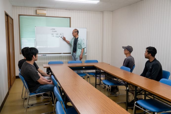 ホワイトボードの前に立ち、着席した職員へ向けて話す男性